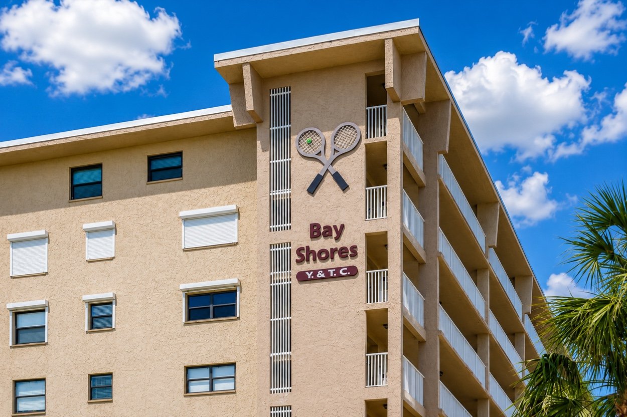 The Bay Shores Yacht and Tennis Club sign on the side of the building, with its crossed-rackets emblem