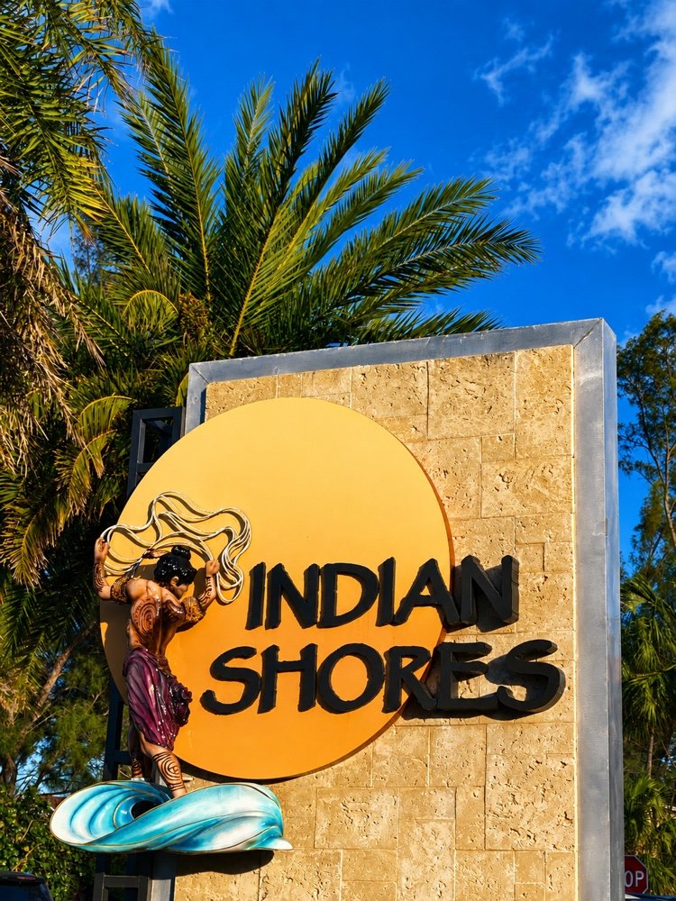 The Indian Shores town sign, a mermaid emblem on a stone wall beneath palms