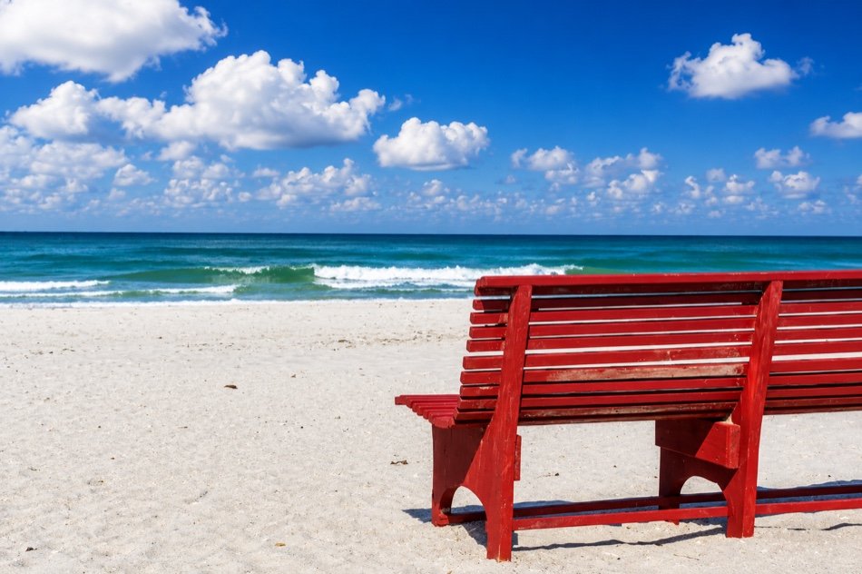 A red bench on the white sand, close up, facing the surf