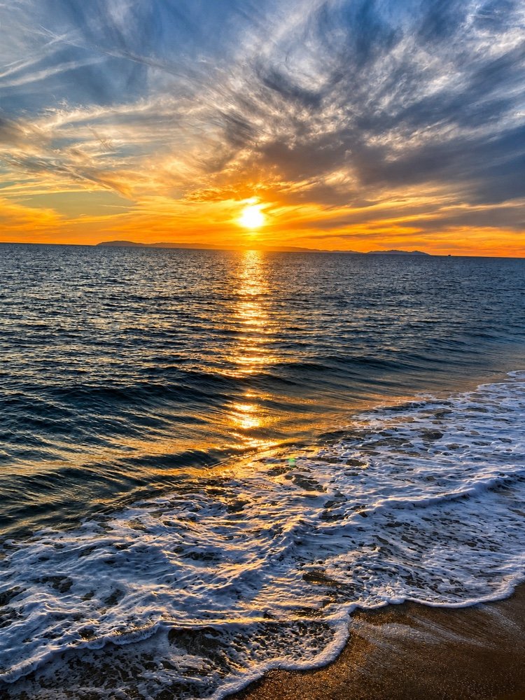 Sunset over the water, with surf running up the sand
