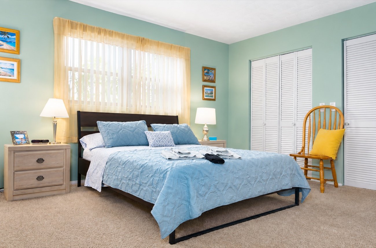 Bedroom one: a queen bed with a blue quilt, lamps either side and a bright window