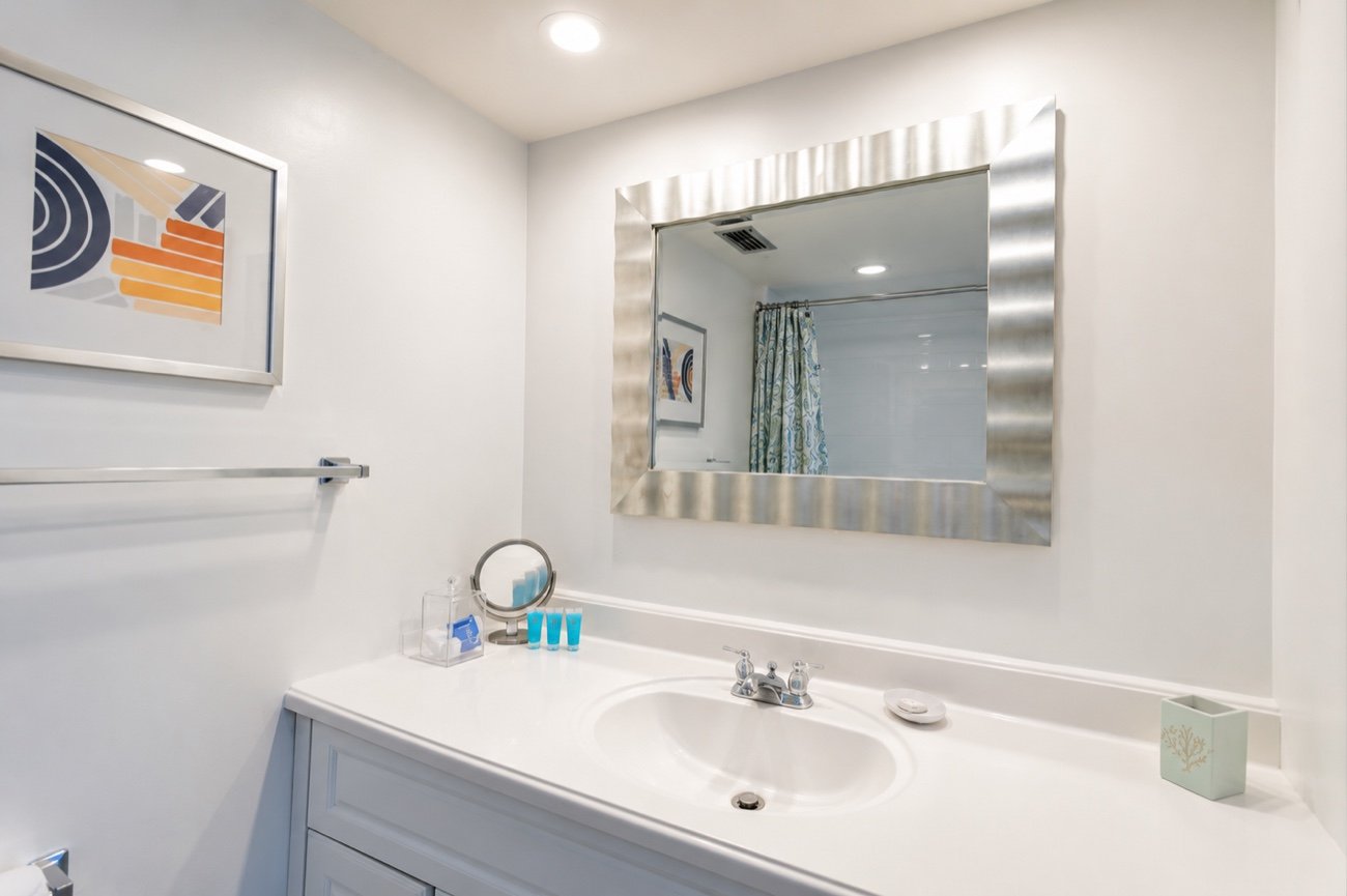 A bathroom vanity with a wide mirror and a walk-in shower reflected behind