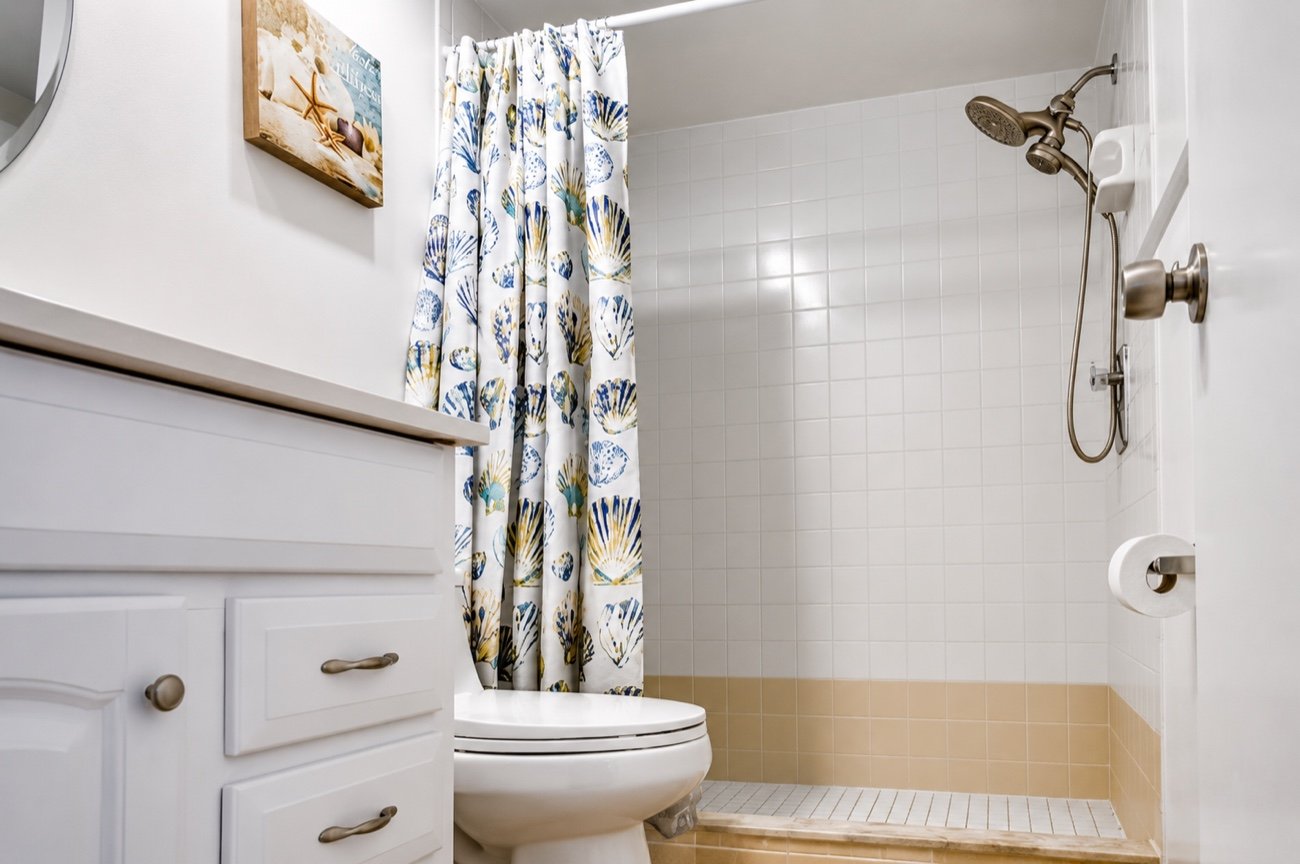 The second bathroom, with a tiled shower over the tub and a shell-print curtain